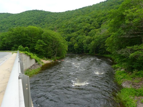 A serene river flows through lush green mountains, with a few kayakers visible in the distance.