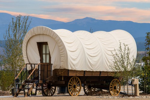 A covered wagon with a white canvas top, set against a backdrop of mountains and a colorful sky.