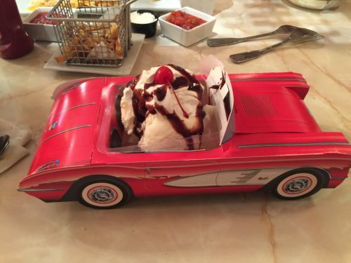 A red convertible car-shaped dessert dish filled with ice cream, topped with chocolate sauce and a cherry.
