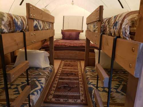 Interior of a cozy tent with two bunk beds and a double bed, featuring patterned bedding and a decorative rug.