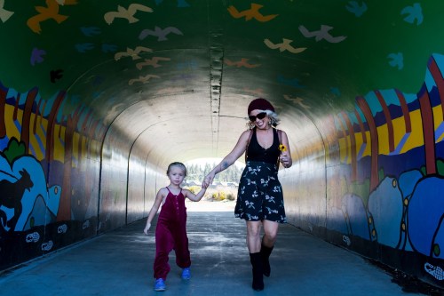 A woman and a child walk hand in hand through a colorful tunnel with painted birds and nature scenes.