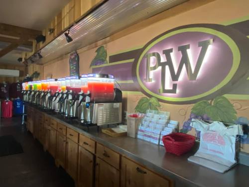 A beverage station with multiple dispensers of colorful drinks, set against a grape-themed mural.