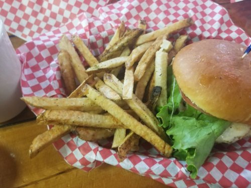 A basket of golden fries next to a burger with lettuce on a red and white checkered paper.
