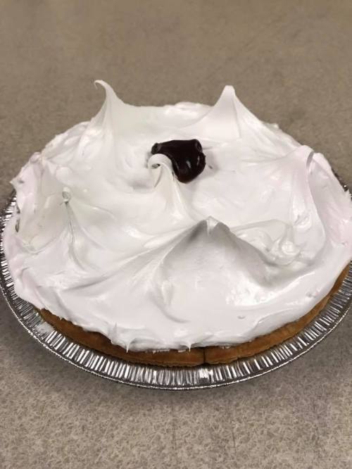 A pie with a fluffy white meringue topping and a small chocolate swirl in the center, set in a silver pie dish.