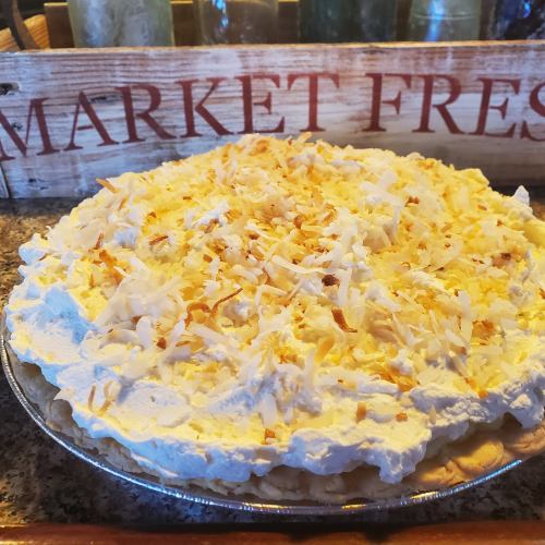 A coconut cream pie topped with whipped cream and toasted coconut flakes, placed on a rustic wooden surface.