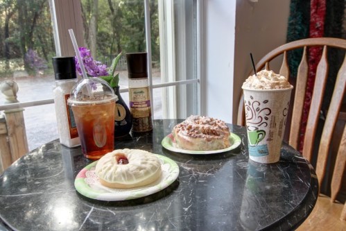 A table with a drink, a dessert, and a pastry, set by a window with greenery outside.