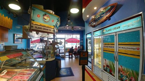 Interior of an ice cream shop with colorful decor, display cases, and seating area visible through large windows.
