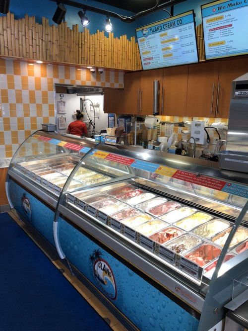 A colorful ice cream shop display with various flavors in glass cases and a menu board above.