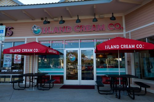 Exterior of Island Cream Co. with red umbrellas over tables, showcasing a welcoming entrance and open sign.