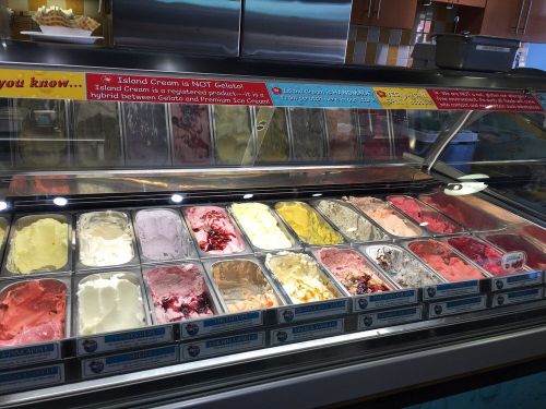 A display of various colorful ice cream flavors in metal tubs at an ice cream shop.
