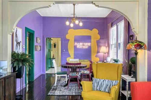 A vibrant living space with purple walls, a yellow frame mural, colorful furniture, and a cozy atmosphere.