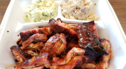 A takeout container with BBQ ribs, coleslaw, and potato salad.