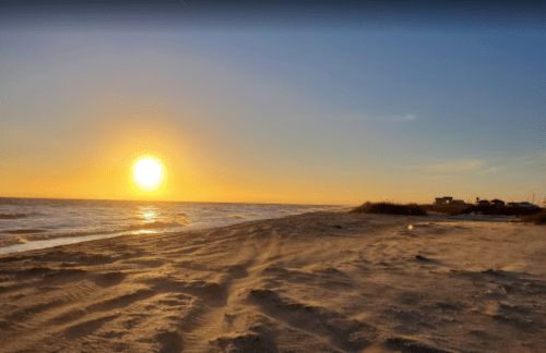 A serene beach at sunset, with golden light reflecting on the water and gentle waves lapping at the shore.