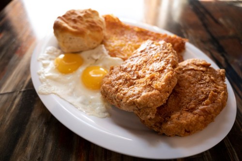 A plate of fried chicken, two sunny-side-up eggs, a biscuit, and a slice of golden hash browns.