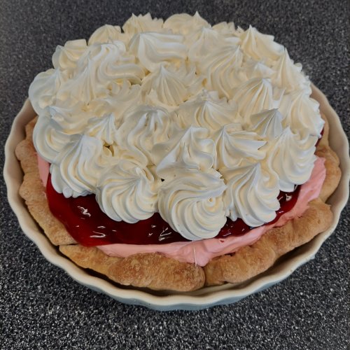 A pie with a flaky crust, filled with pink filling and topped with swirls of whipped cream and cherry topping.