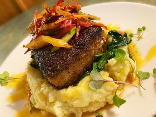 A beautifully plated dish featuring seared fish atop creamy mashed potatoes, garnished with sautéed vegetables and microgreens.