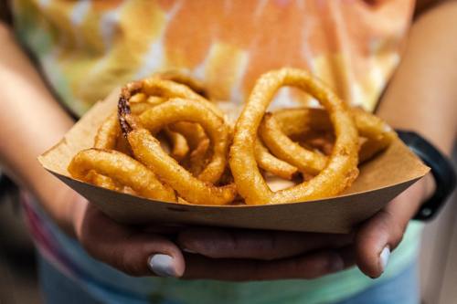 A person holding a tray of golden, crispy onion rings.