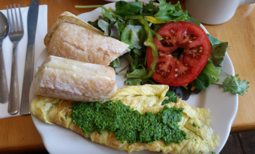 A plate with a green pesto omelette, two bread rolls, and a side salad with tomato slices.