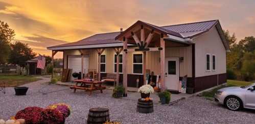 A cozy house with a porch, surrounded by gravel, flowers, and a sunset sky in the background.