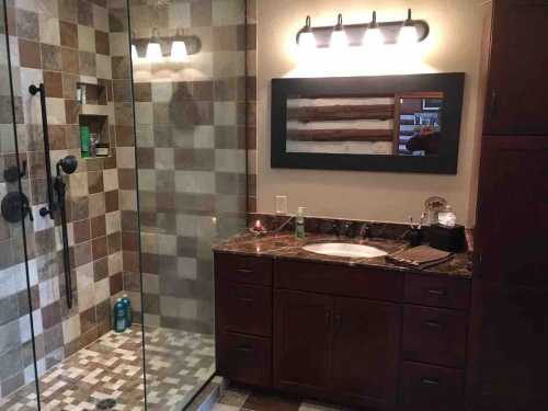 Modern bathroom featuring a glass shower, tiled walls, a double sink vanity, and stylish lighting.