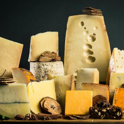 A variety of cheeses displayed on a dark background, including blocks, wedges, and slices, with some nuts and dried fruits.