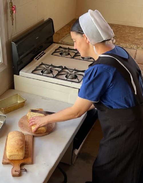 A woman in traditional attire slices freshly baked bread in a cozy kitchen with a gas stove.