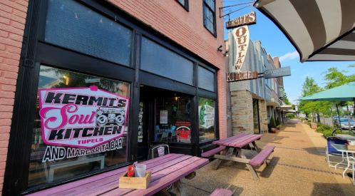 Exterior of Hermit's Soul Kitchen with outdoor seating and a sign for Outlaw Kitchen in a vibrant downtown area.