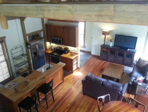 A cozy, modern living space with wooden beams, a kitchen, and a comfortable seating area. Natural light fills the room.