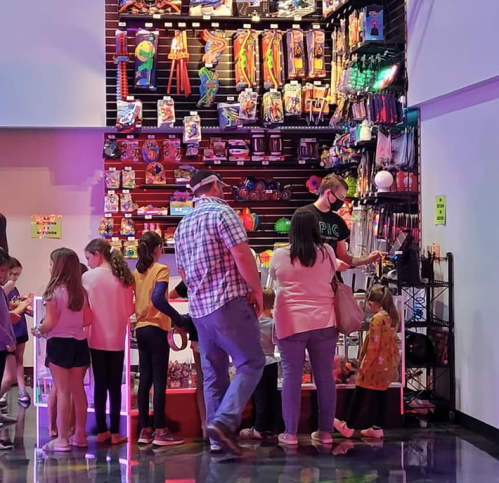 A group of children and adults browse colorful toys in a vibrant store, with shelves filled with various items.