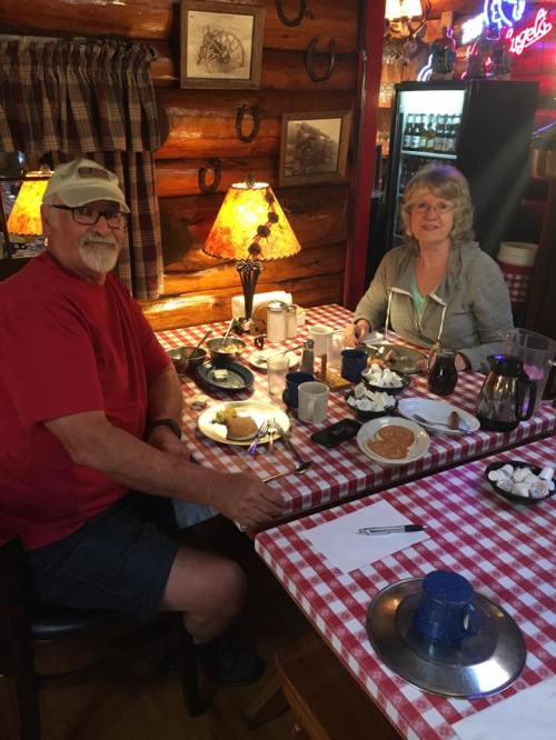 A man and woman sit at a table in a cozy restaurant, enjoying breakfast with coffee and pancakes.