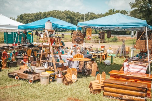 A vibrant outdoor market scene with blue tents showcasing various vintage items and crafts on display.