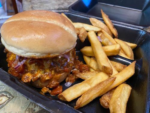 A close-up of a burger with sauce and onions, served with a side of golden French fries in a black takeout container.