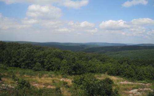 A panoramic view of rolling green hills under a partly cloudy sky.