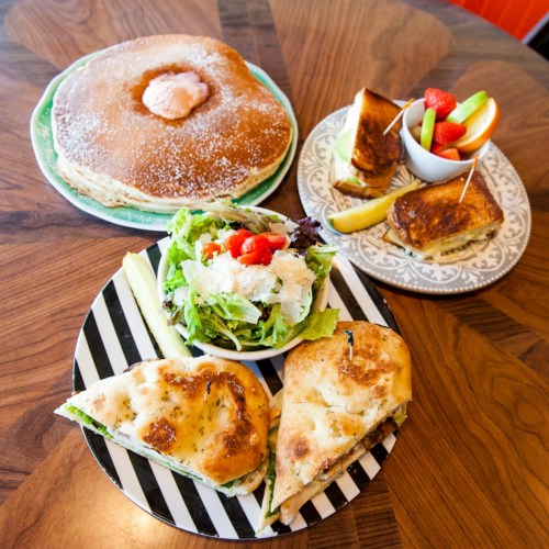 A table with a large pancake, grilled cheese sandwiches, a salad, and a fruit platter.