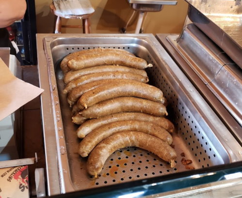 A tray of cooked sausages resting in a metal container with holes, placed on a countertop.