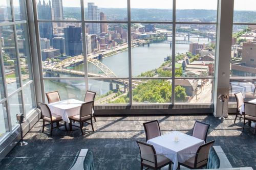 A panoramic view of a city skyline and river from a high-rise restaurant with empty tables.