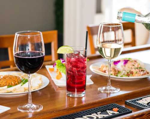 A table setting with red wine, white wine, and a cocktail garnished with lime, alongside plates of food.