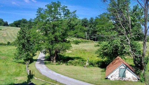 A scenic view of a winding road leading to a small, rustic house surrounded by lush greenery and trees.