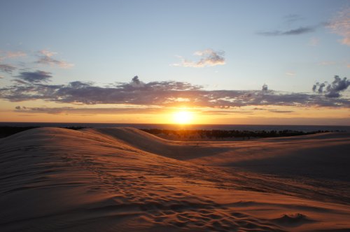 A serene sunset over rolling sand dunes, with soft clouds and a vibrant sky reflecting warm colors.
