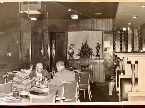 A vintage black-and-white photo of a restaurant interior with diners at tables and decorative sculptures in the background.