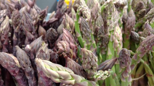 A close-up of fresh asparagus spears, featuring a mix of green and purple varieties.