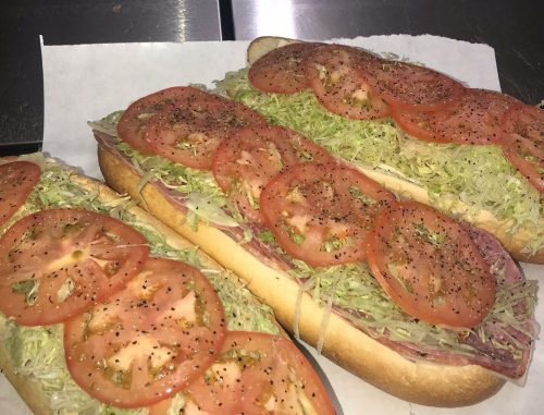 Three sub sandwiches filled with layers of lettuce and tomato slices, resting on a white paper.