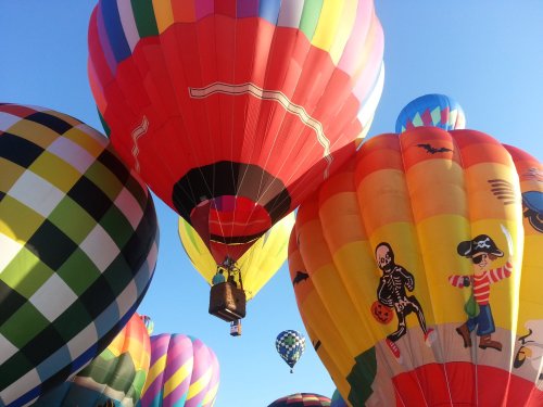 Colorful hot air balloons in various designs float against a clear blue sky, creating a vibrant festival atmosphere.