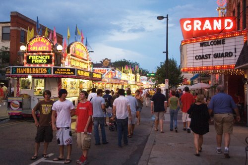 A lively street fair with food stalls, colorful lights, and crowds of people enjoying the festivities at dusk.