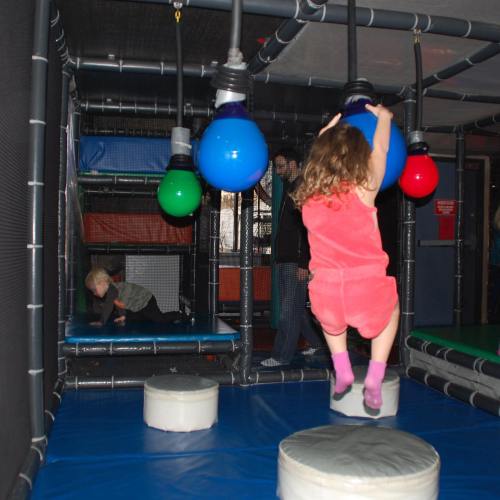Children playing in a colorful indoor play area with hanging balls and soft seating.