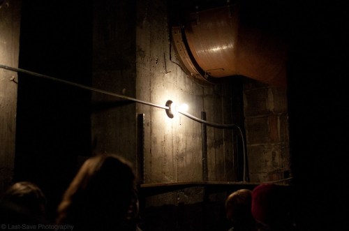 A dimly lit underground space with a single light bulb illuminating a concrete wall and pipes.