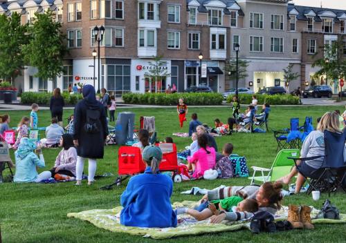 People relax on blankets in a park, enjoying a community event with families and friends gathered on the grass.