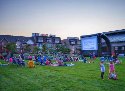 Outdoor movie screening in a park, with families sitting on blankets and chairs as the sun sets.