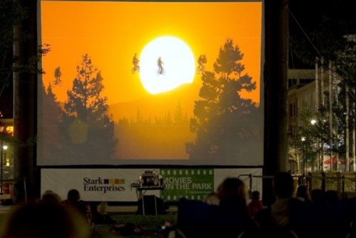 Outdoor movie screening at sunset, featuring silhouetted figures on bicycles against a vibrant orange sky.
