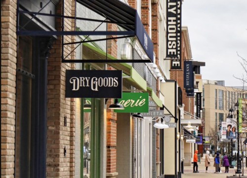 A street view featuring various storefronts, including "Dry Goods" and "Aerie," with pedestrians walking by.